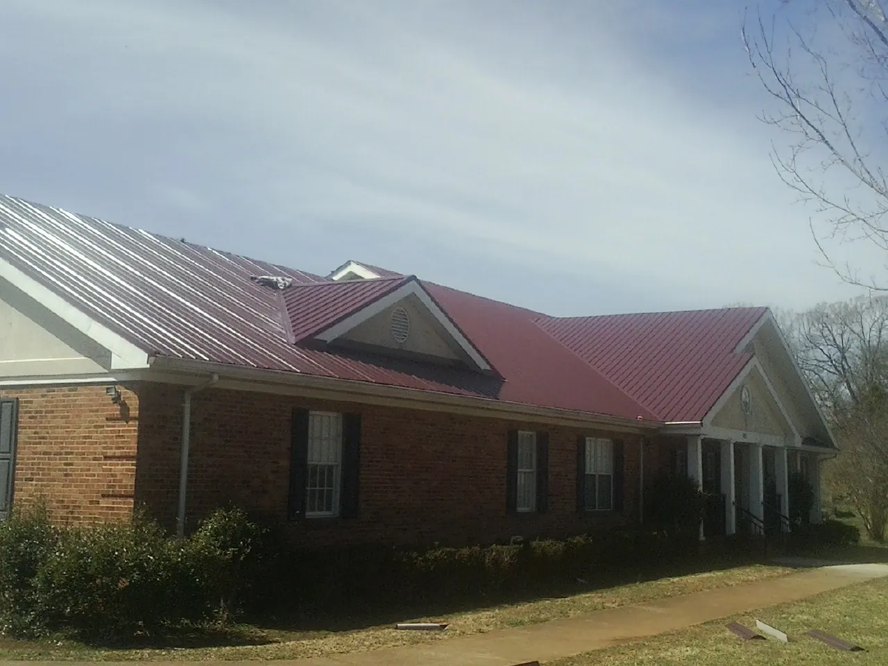 Red metal roof with gabled entries on a long brick building, from a Hail Damage Roof Repair job in Elmer