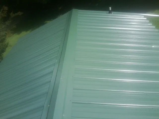 New green metal panels meeting at the ridge of a roof — Flat Roof Repair work by our crew in Elmer