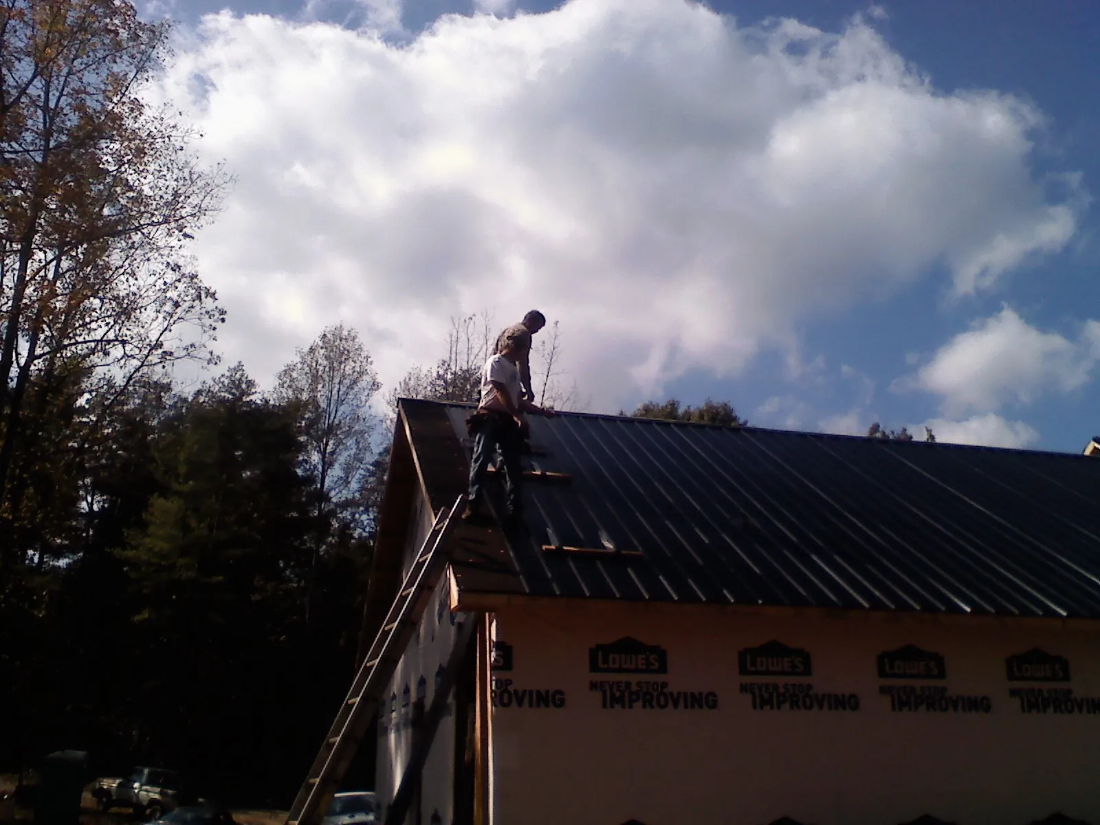 Roofer fastening dark metal panels high against a cloudy sky, from a Roof Inspection job in Elmer
