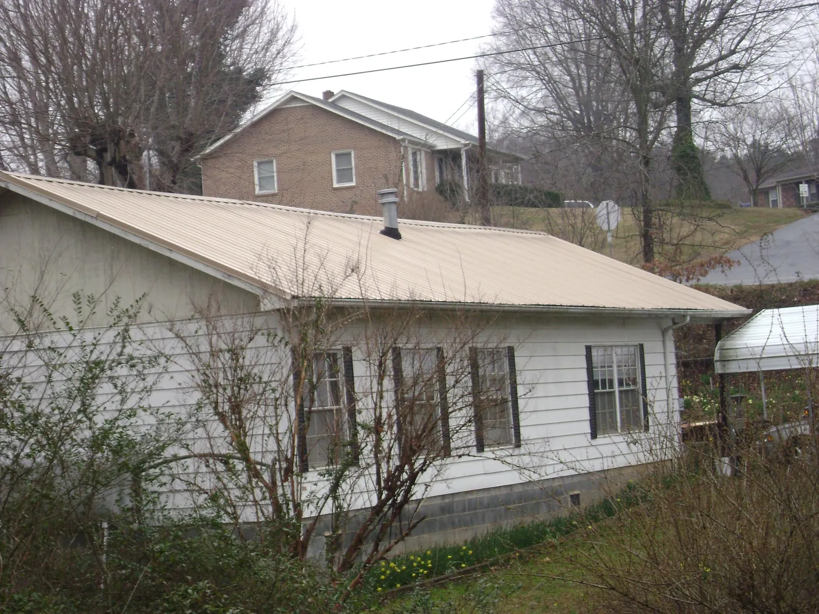 Tan metal roof on a white sided house set into a hillside — Commercial Roofing by Roofing Brothers in Elmer