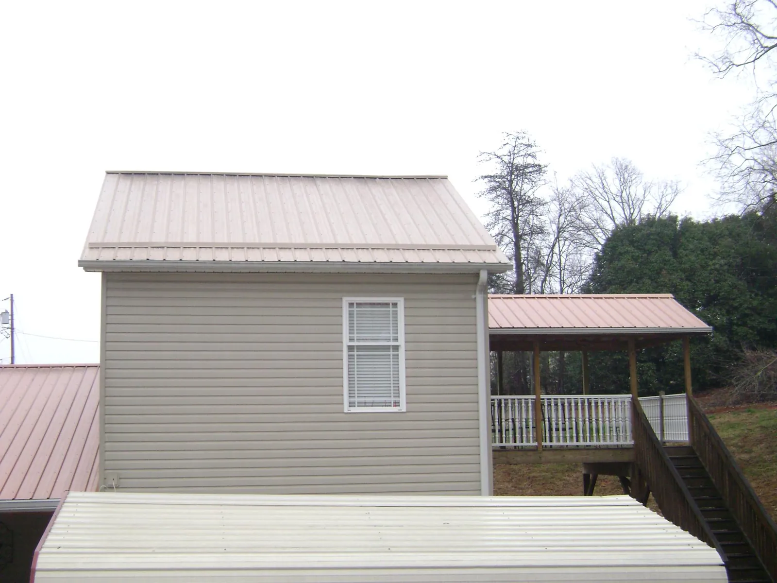 Tan metal roofs on a two story addition and attached porch, from a Roof Replacement job in Elmer